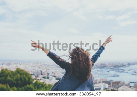 Back view of cheerful young woman with hands up. Freedom concept.