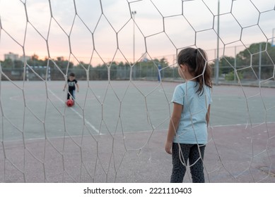 Back View Of Child Goalkeeper Ready To Catch A Soccer Ball Stand On Soccer Field In Football Goal. Selective Focus On Girl.