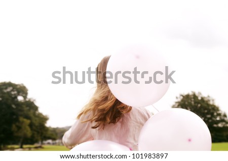 Back view of a child holding balloons in the park.