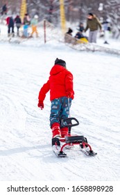 Back view of child in pulling sledge and running up snowy slope while spending time on ski resort