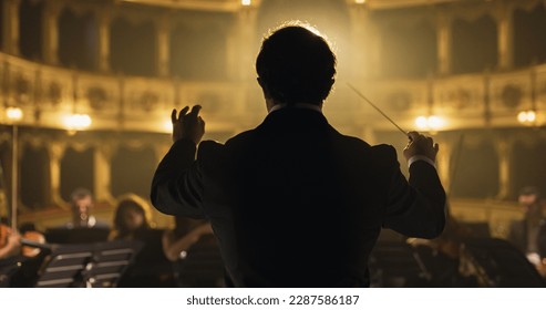 Back View Cinematic shot of Conductor Directing Symphony Orchestra with Performers Playing Violins, Cello and Trumpet on Classic Theatre with Curtain Stage During Music Concert - Shutterstock ID 2287586187