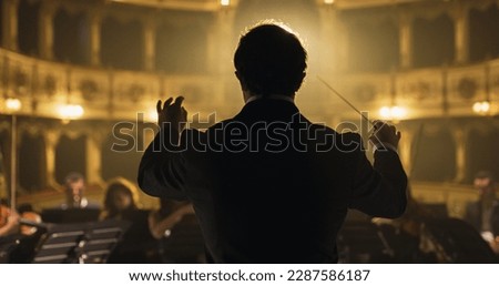 Back View Cinematic shot of Conductor Directing Symphony Orchestra with Performers Playing Violins, Cello and Trumpet on Classic Theatre with Curtain Stage During Music Concert