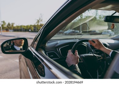 Back view close up cropped up photo young driver reflected in mirror man wearing black suit driving car taxi hold steering wheel look camera Vehicle transport traffic lifestyle business trip concept.