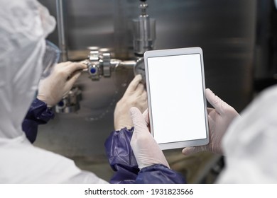 Back view close up of two workers holding tablet with blank white screen at modern chemical plant, copy space
