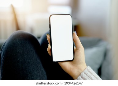 Back View Close Up Of A Woman Hand Holding And Using Smart Phone With White Blank Empty Screen Sitting On A Bed At Home. High Quality Photo