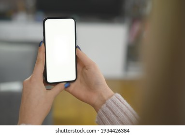 Back View Close Up Of A Woman Hand Holding And Using Smart Phone With White Blank Empty Screen Sitting On A Bed At Home. High Quality Photo