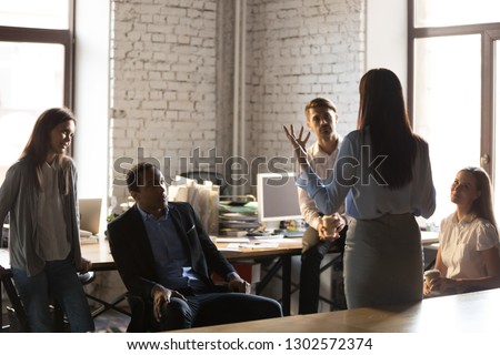 Back view of confident businesswoman standing in front of colleagues, gesturing talking about business ideas or projects, female team leader hold briefing or informational meeting with employees