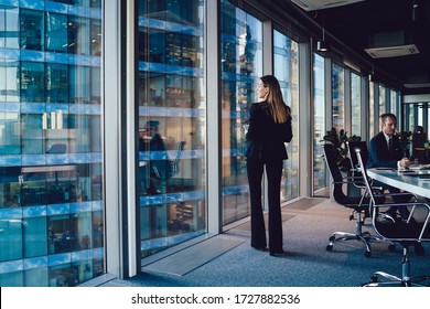Back view of confident female in elegant suit standing near window in office with panoramic view on business buildings pondering about career, prosperous woman in formal outfit thinking about job