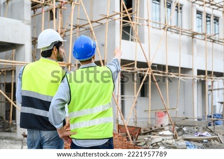 Back view of Construction engineer and architect check plan working with the blueprint on construction site. They are in safety vests with helmets for safety. Construction project concept