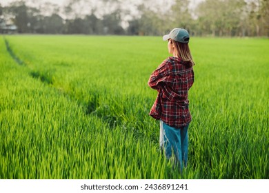 Back view of a contemplative female farmer looking over a vast, green paddy field at the end of the day. - Powered by Shutterstock