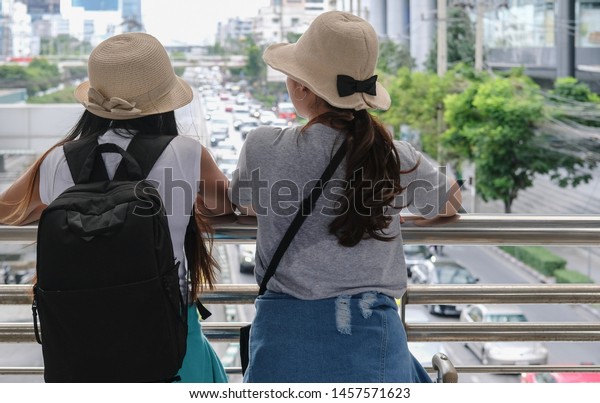 Back view of couple asian woman travelers are\
sightseeing at Bangkok city among traffic jam on the road in the\
afternoon with copy space.
