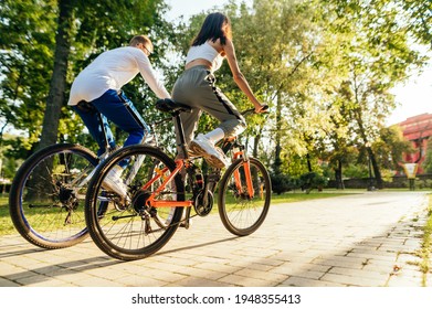 Back view of a couple of fashionable sportsmen, a male and female, riding their bicycles in the city park, staying fit and sporty. - Powered by Shutterstock