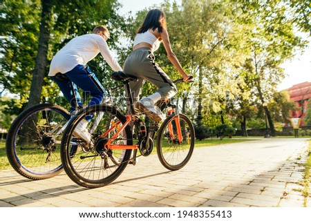 Back view of a couple of fashionable sportsmen, a male and female, riding their bicycles in the city park, staying fit and sporty.
