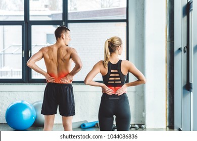 back view of couple having backache after workout in gym