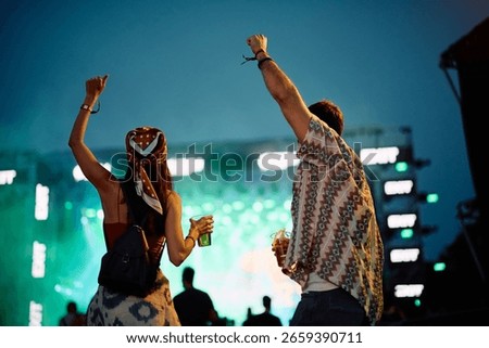 Back view of couple having fun at open air music concert at night.