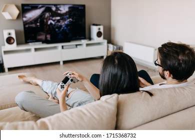 Back view of a couple of man and woman playing video game on a console, sitting on couch in living room. - Shutterstock ID 1715368732