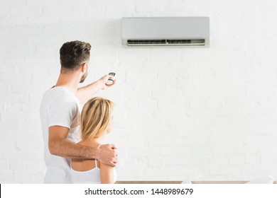back view of couple with remote control suffering from heat under air conditioner at home