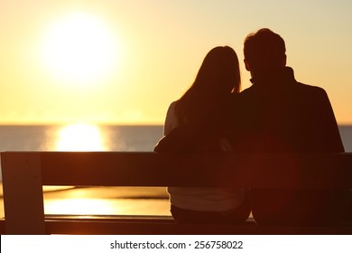 Back view of a couple silhouette hugging and watching sun on the beach 