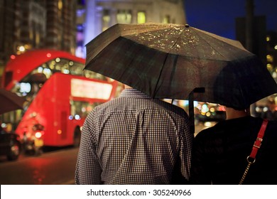 Back view of couple under the umbrella in the evening against the double-decker in London. Image with selective focus