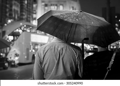 Back view of couple under the umbrella in the evening against the double-decker in London. Black-and-white image with selective focus