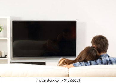Back view of a couple watching tv in a couch at home. Blank screen view