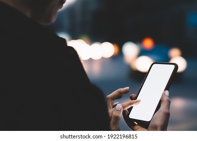 Back view of crop faceless female wearing black jacket using mobile phone while standing in city street near roadway with cars - Powered by Shutterstock