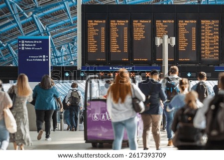 Back view of a crowd of commuters walking toward the platforms, with the train timetable above at London Waterloo station