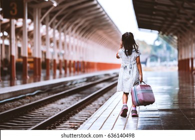 Back view of cute asian little girl holding suitcase and walking on a railway station in vintage retro style