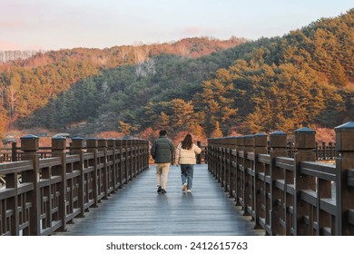 Back view cute couple walking by woryeonggyo Bridge, Wooden bridge at Andong, South Korea on autumn season. Andong couple trip. Vanishing point and symmetrical shot with a forest at background - Powered by Shutterstock