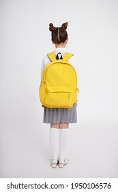 Back View Of Cute Girl In School Uniform With Big Yellow Backpack Posing Over White Background