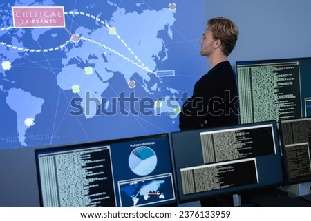 Back View in the Cyber Security Control Center Operator Working. Multiple Screens Showing Technical Data and Alerts.