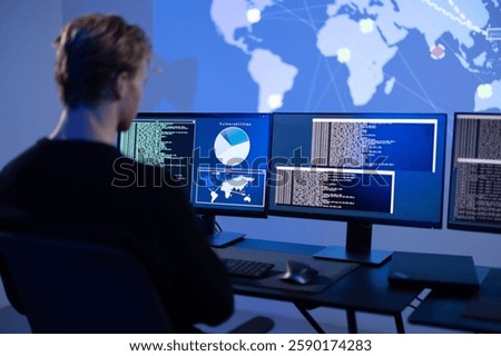 Back View in the Cyber Security Control Center Operator Working. Multiple Screens Showing Technical Data and Alerts.