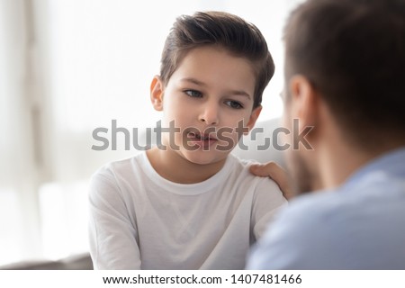 Back view of dad sit on couch with preschooler son talking sharing thoughts or problems, loving father speak have conversation with little boy child, support him showing care and understanding