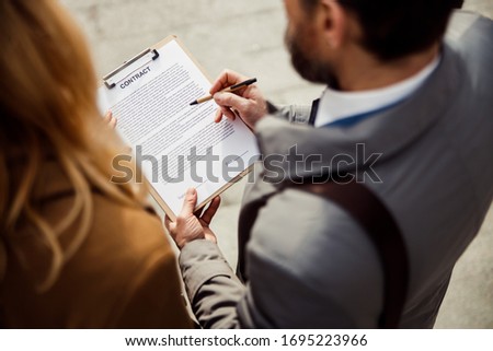 Back view of a dark-haired man and a blonde Caucasian woman scrutinizing a contract outdoors