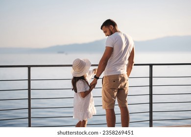 Back view of daughter with her father stand on heigh balcony in front of sea sunset. Dad with his little girl looking on mountains - Powered by Shutterstock