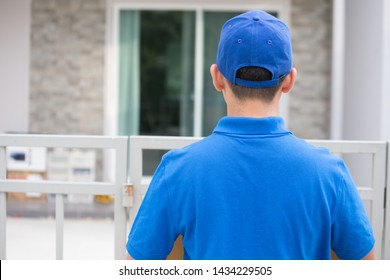 Back view of delivery man holding parcel box standing in front of the house