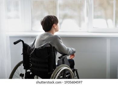 Back view of disabled teenager in wheelchair looking out window, having depression at home, copy space - Powered by Shutterstock