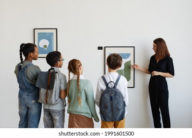 Back View At Diverse Group Of Children Listening To Female Tour Guide While Visiting Modern Art Gallery, Copy Space