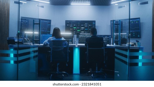 Back view of diverse IT technical specialists working on computers with database server in modern monitoring office at night. Big digital screens with real-time analysis charts and blockchain network.