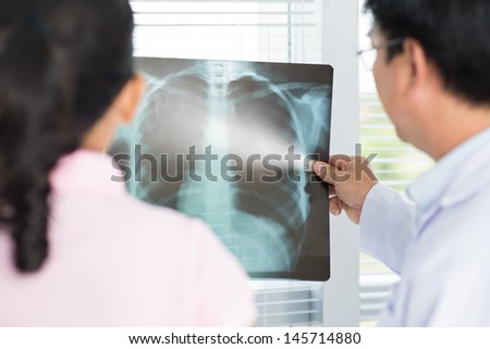 Back view of a doctor and a patient examining an x-ray together
