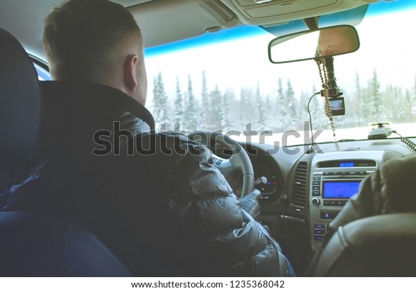 Back view of  driver  in winter jacket driving\
through winter forest