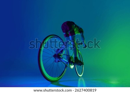Back view dynamic image of man, cyclist in motion on bicycle, training against blue background with green neon light. Concept of sport, competition, active lifestyle, endurance
