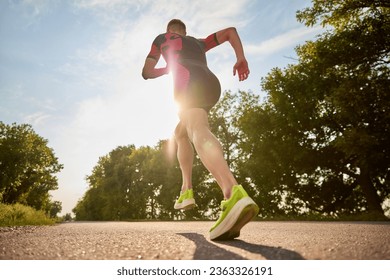 Back view dynamic image of sportsman, runner in sportswear training, running alone the road. Concept of professional sport, triathlon preparation, competition, athleticism - Powered by Shutterstock