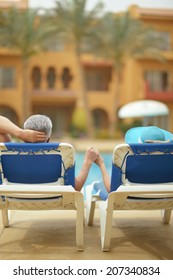 Back View Of Elderly Couple Lying By Pool At Hotel Resort