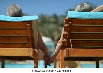 Back View Of Elderly Couple Lying By Pool At Hotel Resort