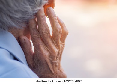 Back View Of Elderly Woman Hand Touch In The Ear Her. Focus On Hands Wrinkled Skin. Health Care Concept