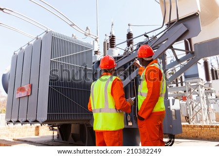back view of electricians standing next to a transformer in electrical power plant