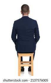 back view of elegant grizzled man sitting on wooden chair in front of white background in studio
