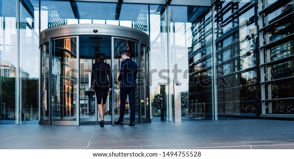 Back view of elegant man and woman\
walking into round revolving doors while entering contemporary\
glass skyscraper building of corporation\
office