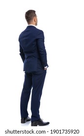 back view of elegant young businessman in navy blue suit holding hands in pockets and standing isolated on white background in studio